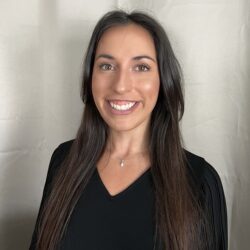 A person with long dark hair and a black top smiles at the camera against a neutral background, embodying the essence of Care Initiative.