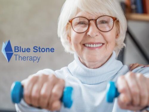 An elderly woman with short white hair and glasses smiles while holding blue dumbbells, supported by a young woman in a blue uniform. The logo Blue Stone Therapy is visible on the left side, highlighting their Care Initiative.